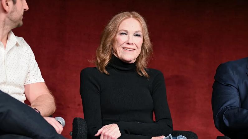 Catherine O'Hara smiles while wearing a black turtleneck.