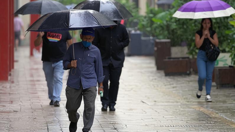 Pedestres se protegem da chuva na Praça Dom José Gaspar, na região central de São Paulo, Brasil.