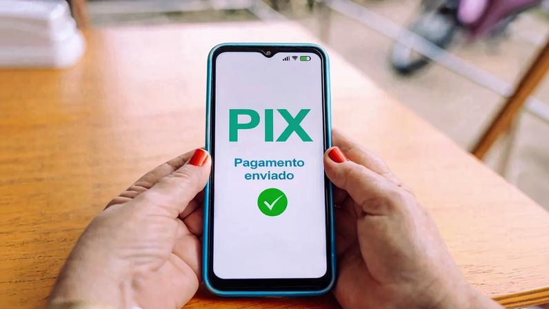 Hands holding a smartphone displaying a payment confirmation via Pix, illustrating the evolution of digital and cashless payment methods