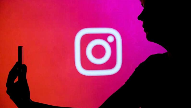 Silhueta de um homem segurando o celular na frente de um painel com o logo do Instagram.