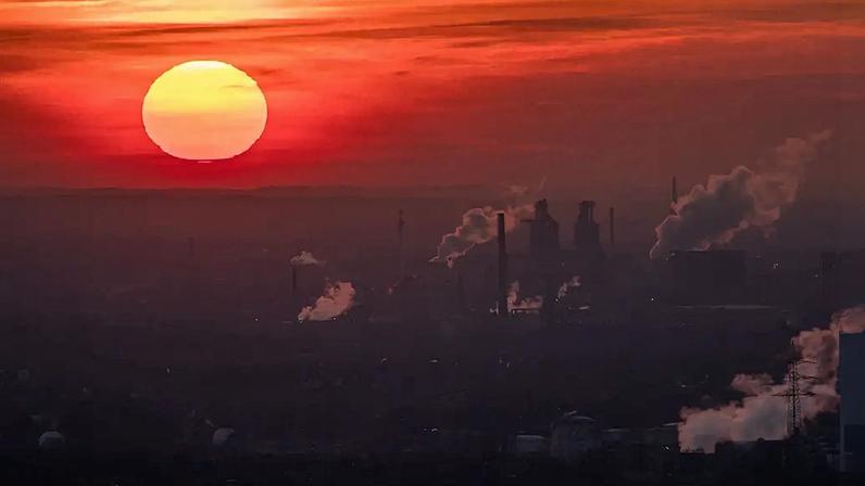 Fotografia de um sol vermelho, na cidade vapor e gases de escape sobem de diferentes empresas em um frio dia de inverno.