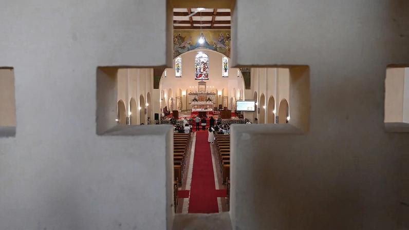 A cross-shaped opening shows nuns holding school lessons — a long red carpet extends forward into a church.