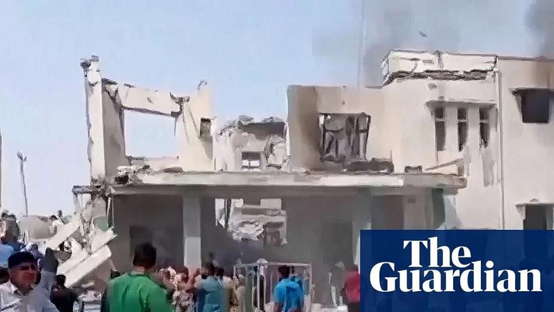 People crowd around a destroyed building as smoke rises from it