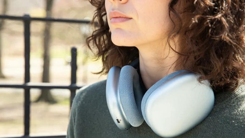 The blue Apple AirPods Max 2 around a person’s neck while outside.