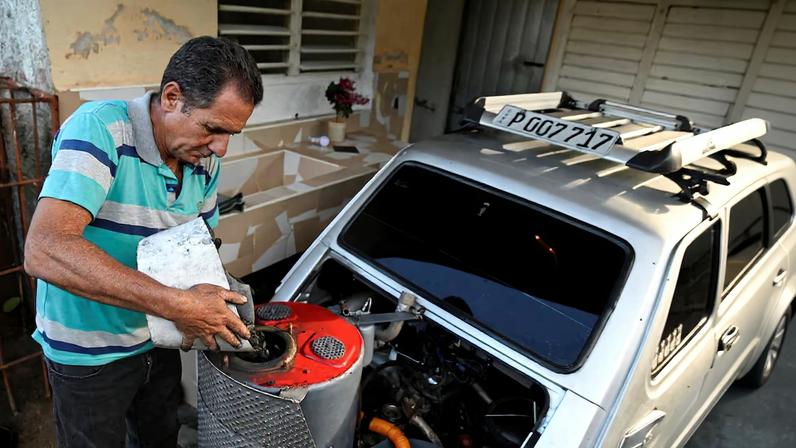 Cuban mechanic Juan Carlos Pino, 56, puts charcoal into the fuel tank to fuel his modified 1980 Polish‑built Polski car, adapted to run on charcoal, a cheaper and more abundant alternative to gasoline since the United States cut off oil shipments to the Caribbean Island, in Aguacate, Cuba, March 16, 2026. REUTERS/Norlys Perez