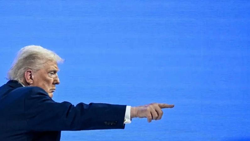 Trump is shown from the side as he points forward with his right arm.