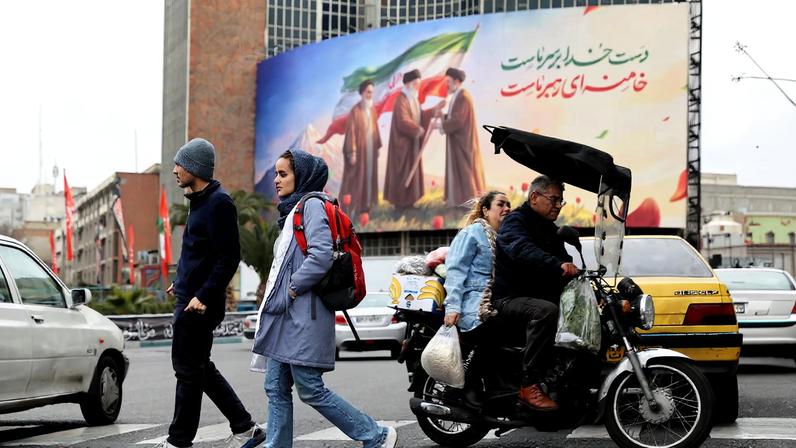 People walk on a street with a banner of Iran's new supreme leader Mojtaba Khamenei with late supreme leader Ayatollah Ali Khamenei, in Tehran