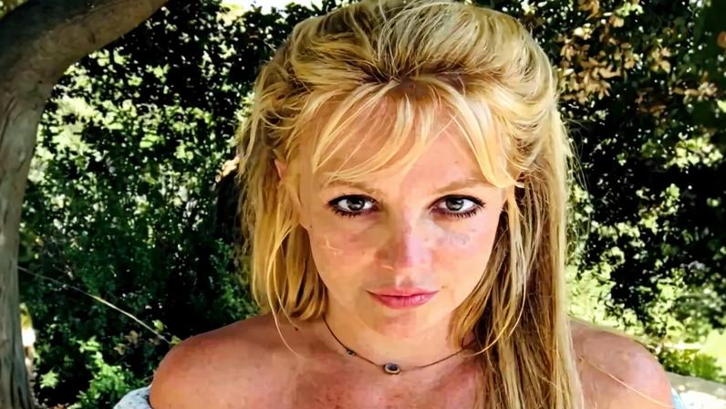 Britney Spears looking at the camera wearing a white off-the-shoulder floral crop top.