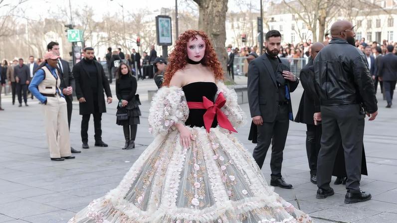 Chappell Roan attends the Valentino show in a dramatic black and cream gown with red bow accent and puffy sleeves.