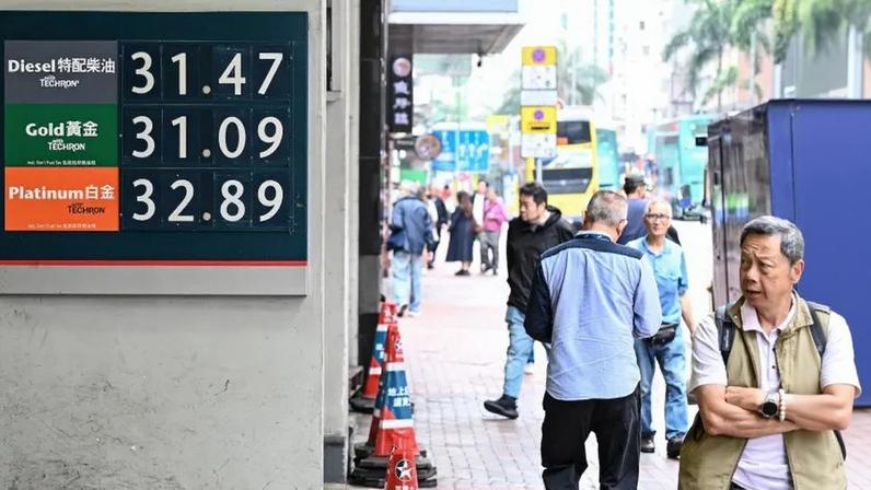 Pedestrians walk past a display with the prices in Hong Kong dollars at a gas station in Hong Kong.