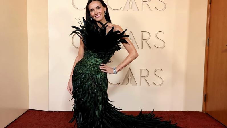Demi Moore in a strapless green and black feather gown poses at the Oscars.