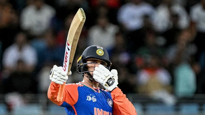 Abhishek Sharma, a player for India's national cricket team, is dressed in official sport attire while holding a bat.