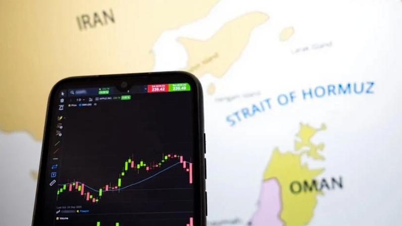 Uma curva da bolsa de valores aparece na tela de um smartphone, enquanto um mapa mostra o Estreito de Ormuz.