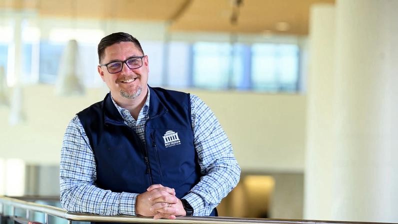 Greg Knutson leans on a balcony railing in a sunlit atrium