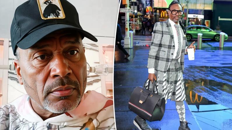 Billy Porter in a plaid suit with a pleated skirt, carrying a bag and a coffee cup on a city street.
