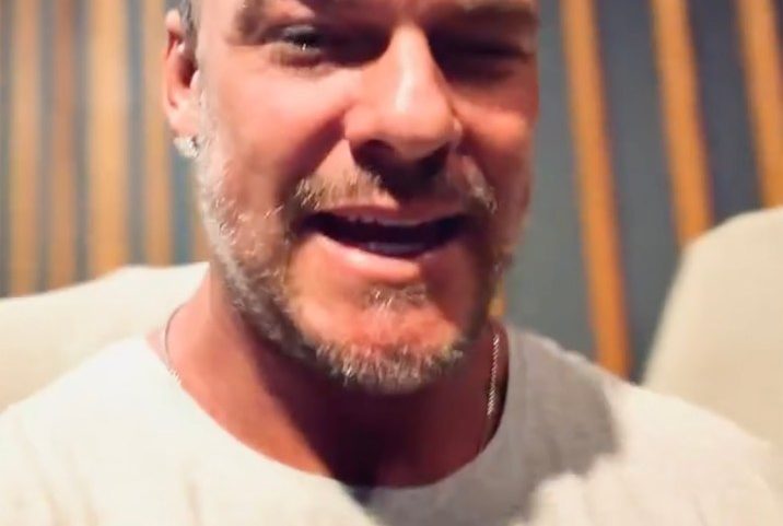 Actor Alan Ritchson, wearing a black cap and white T-shirt, smiling at the camera.