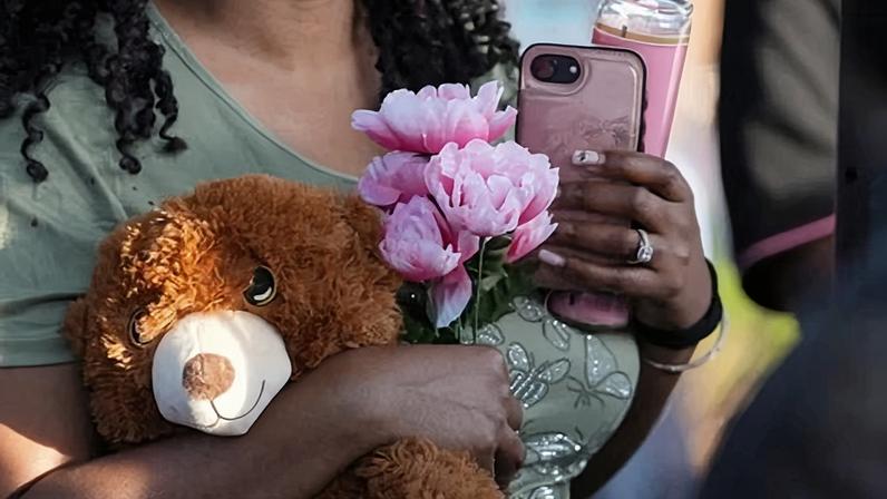 A woman holds flowers and a stuffed toy during a vigil to mourn eight children fatally shot in Shreveport, Louisiana.