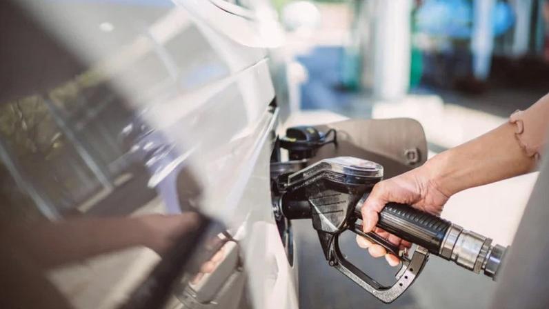 Close-up da mão de uma mulher segurando a bomba de diesel enquanto abastece um carro em um posto de gasolina.