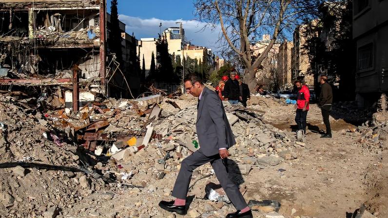 A man in a suit walks near the remains of a residential and commercial building in the Shahrak-e Gharb neighborhood of Tehran.
