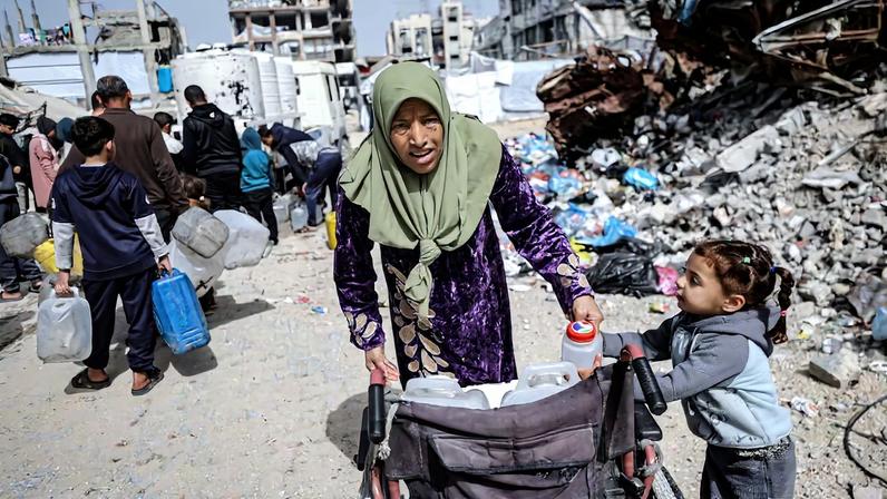 Una mujer y una niña empujan una silla de ruedas cargada con bidones en el asentamiento temporal de Jabalia, en Gaza, este sábado.