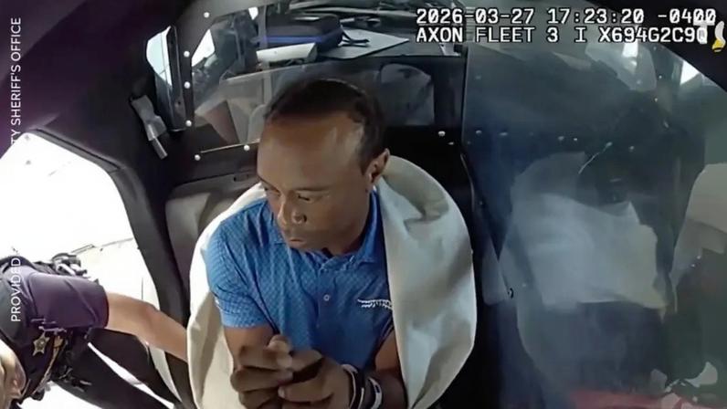 Tiger Woods handcuffed and wrapped in a white blanket in the back of a police car.
