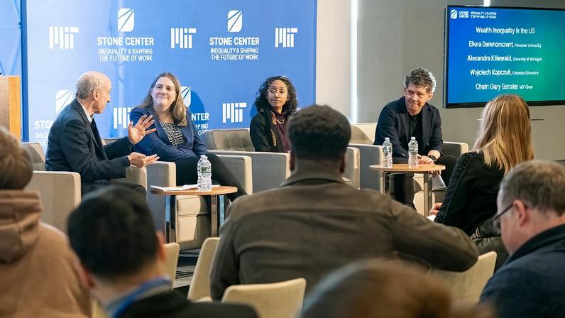 Gary Gensler, Alexandra Killewald, Ellora Derenoncourt, and Wojciech Kopczuk sit in armchairs onstage in front of a blue Stone Center banner