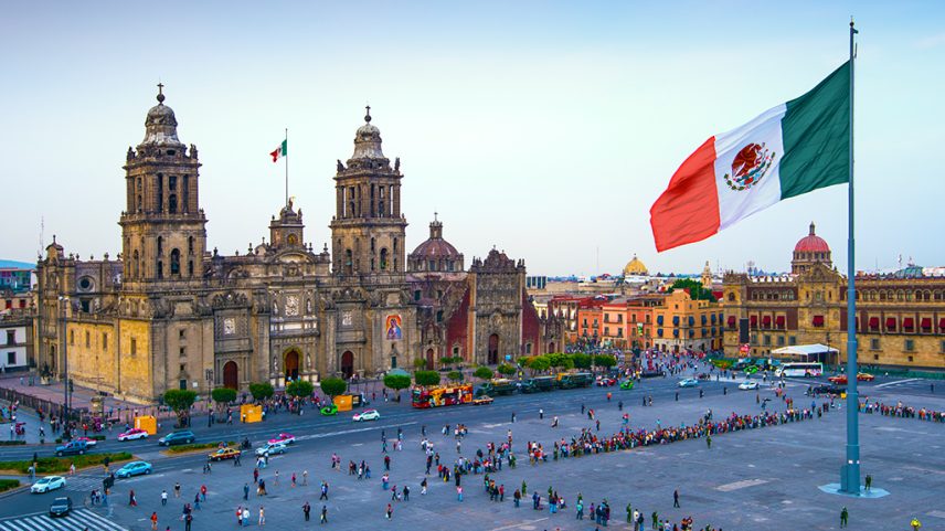 A bandeira mexicana tremula sobre o Zócalo, a praça principal da Cidade do México. A Catedral Metropolitana fica em frente à praça, também conhecida como Praça da Constituição.