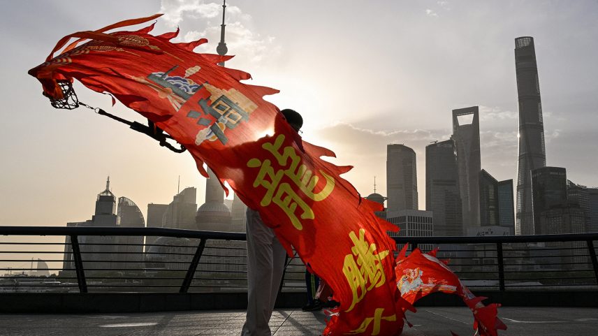 A woman waves a dragon streamer along the Huangpu River, with Shanghai’s financial district behind her, on April 14, 2025.