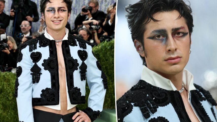 Hudson Williams in a light blue matador-inspired suit with black embroidery and bold, colorful eye makeup.
