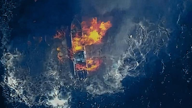 Aerial, color view of fireball above boat on ocean.