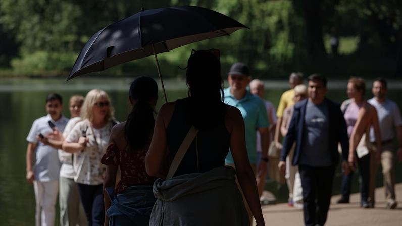 People walking under an umbrella to shelter from the sun in a park