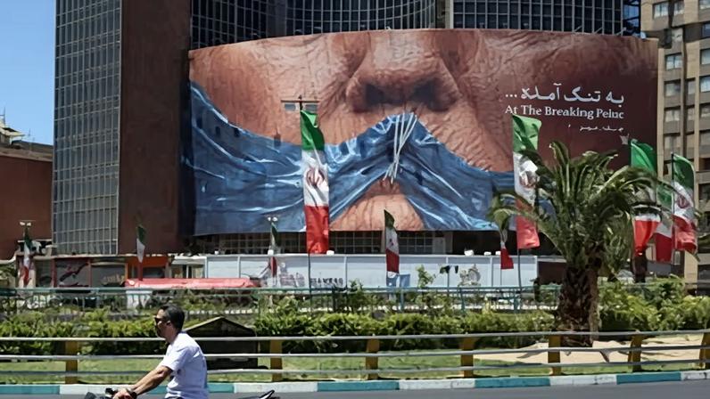 People drive in front of a large anti-US billboard in Tehran.