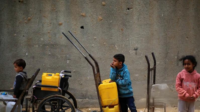 Children with yellow water canisters on trolleys and a wheelchair at a refugee camp. Israel has refused to relax restrictions on ‘dual-use’ items, such as water pipes.