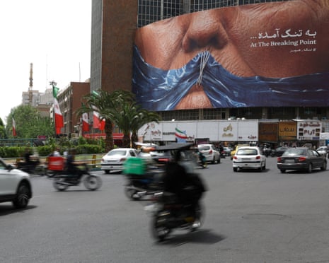 People in Tehran drive past an anti-US billboard depicting Donald Trump and the strait of Hormuz.