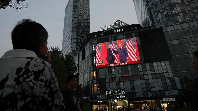 A woman watches a news program about the meeting between U.S. President Donald Trump and Chinese President Xi Jinping, seen on a giant screen outside a shopping mall in Beijing on May 14.