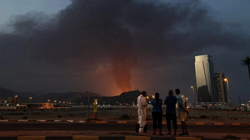 Foreign workers look at a tall plume of black smoke ascends following an explosion in the Fujairah industrial zone on March 3, 2026.