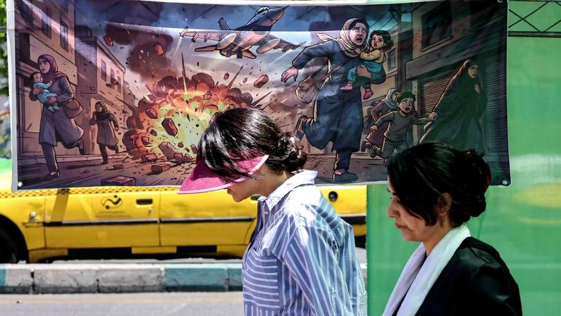 Women in Tehran are seen walking on the street past a banner that depicts U.S. and Israeli strikes on Iran.