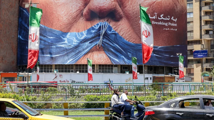 Motorists in Tehran drive their vehicles past a political billboard featuring U.S. President Donald Trump and the Strait of Hormuz.