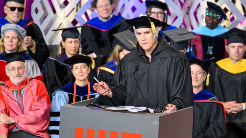 Alejandro Aravena stands at an indoor MIT lectern. MIT faculty members sit behind him. All wear academic regalia.