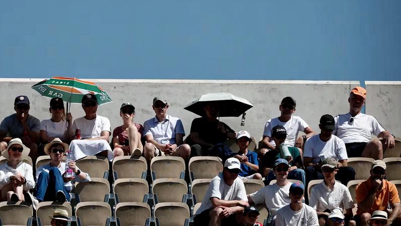 Espectadores del torneo Roland Garros se protegen del calor con parasoles.