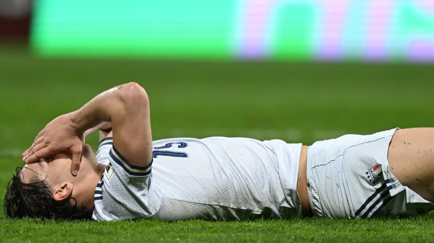 Imagem de um jogador de futebol da seleção italiana deitado no gramado com as mãos no rosto.