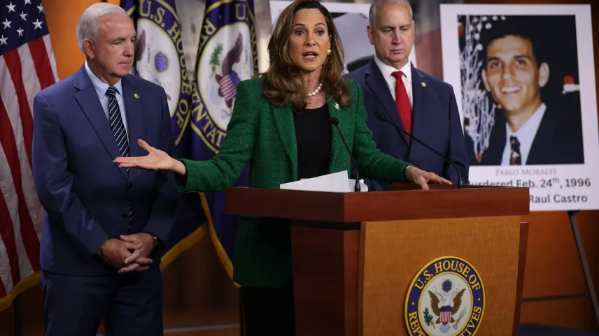 U.S. Republican Rep. Maria Elvira Salazar speaks at a lecturn while flanked to her right by a large picture of one of the U.S. pilots who was fatally shot down by Cuban jets in 1996 as well as by Republican Rep. Mario Díaz-Balart , standing to her right, and by Republican Rep. Carlos Gimenez standing to her left.