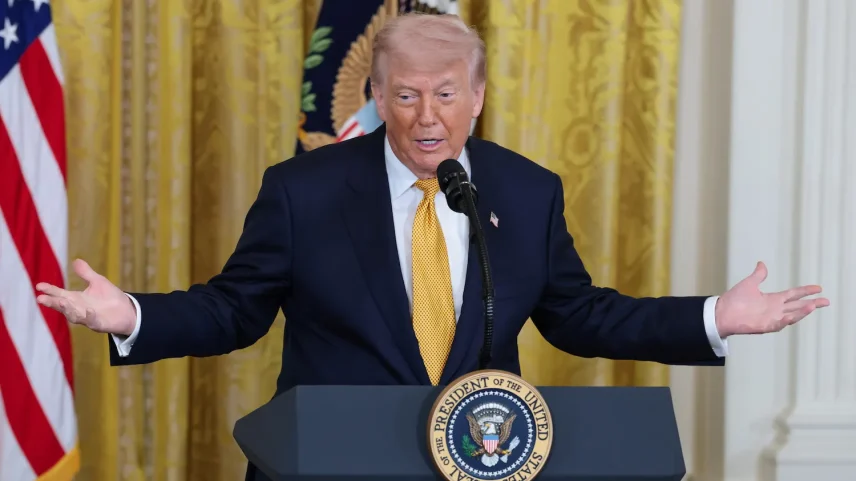 U.S. President Donald Trump stands in front of a podium bearing the U.S. presidential seal. He speaks into a microphone while holding up both hands.