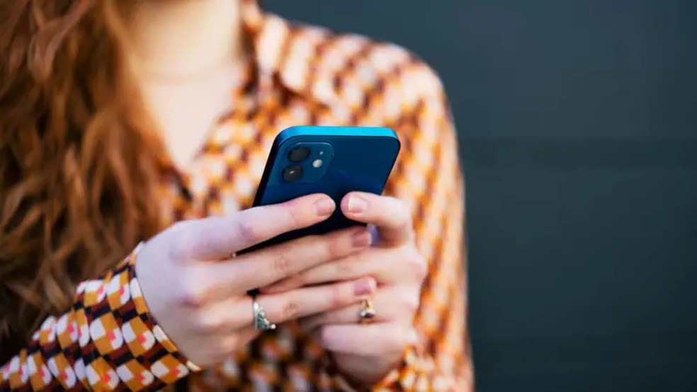 Getty Images A smartphone being read, held in the hands of a woman with long, wavy, red hair and wearing a brown, orange, white and red-patterned shirt.