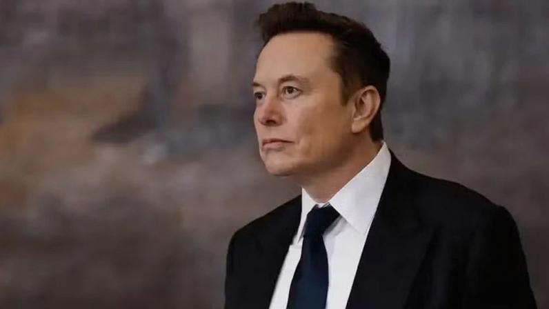 Getty Images Elon Musk wearing a black suit, white shirt, and black tie looking into the distance