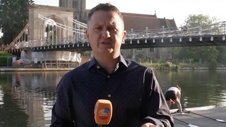 Weather presenter Matt Taylor reporting near a river and bridge