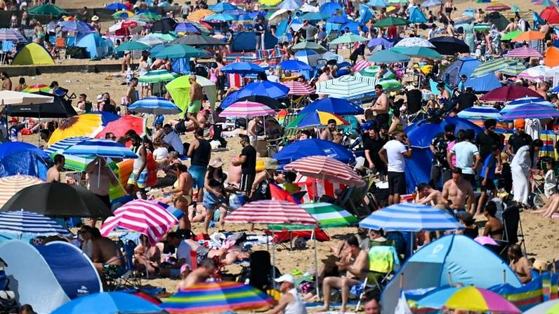 A Bournemouth beach full of people sitting under brightly-coloured sun umbrellas.