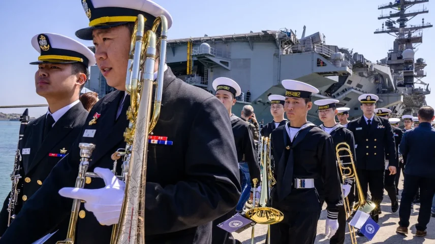 South Korean Navy band members walk past the USS Nimitz aircraft carrier during its port visit to Busan, South Korea, on March 28, 2023.