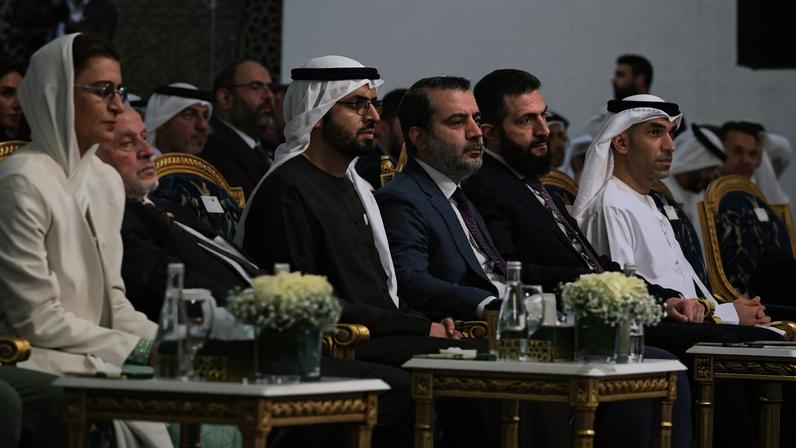 A few dozen officials sit side by side in ornate chairs decorated with gold and upholstery. Some wear Western business suits, while others wear more local formal attire.
