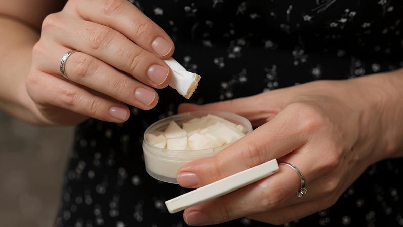 Mãos de mulher com anéis segurando um sachê de nicotina e um pote transparente com outros sachês, em preto e branco